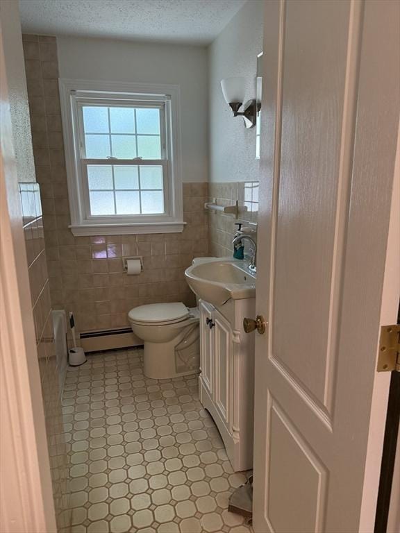 full bath with baseboard heating, tile walls, vanity, toilet, and a tub