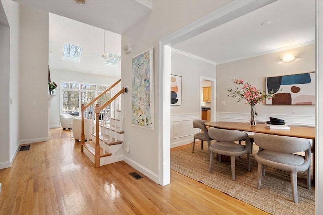 interior space with a skylight, ornamental molding, and light hardwood / wood-style flooring