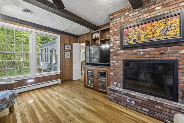 living area with a baseboard heating unit, beamed ceiling, hardwood / wood-style flooring, a brick fireplace, and wood walls