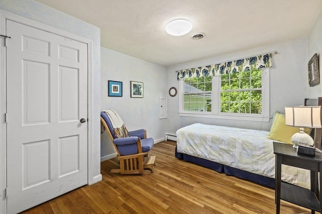 bedroom featuring wood finished floors, baseboard heating, and baseboards