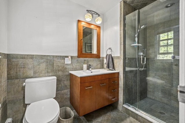 bathroom with tile walls, a stall shower, toilet, vanity, and a wainscoted wall