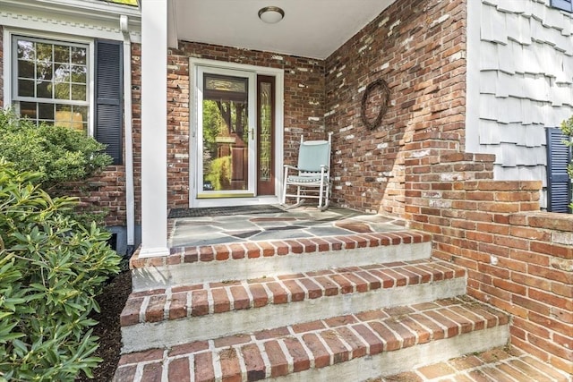 doorway to property featuring a porch and brick siding