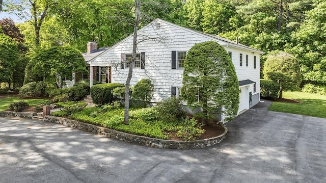 view of property exterior featuring asphalt driveway, a chimney, and a garage