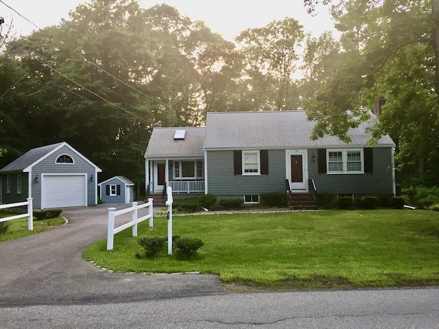 view of front of home with aphalt driveway, a detached garage, a front yard, entry steps, and an outdoor structure