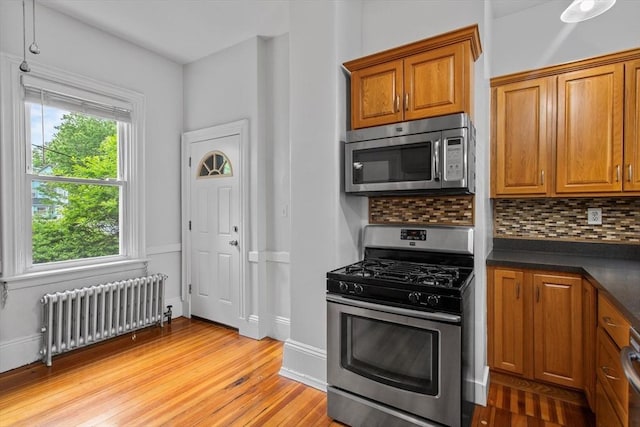 38 Torrey St, Boston, MA 02124 - kitchen featuring stainless steel appliances, radiator, dark countertops, brown cabinetry, and backsplash
