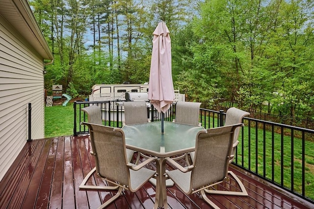 wooden terrace with outdoor dining area, a yard, and view of wooded area