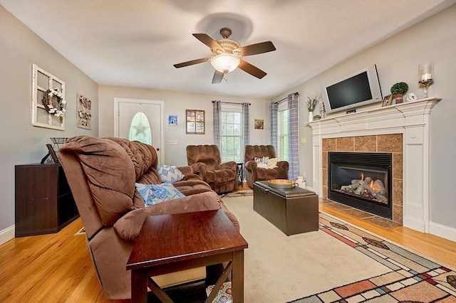 living area featuring light wood-type flooring, a tile fireplace, a ceiling fan, and baseboards