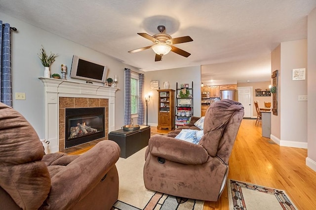 living room featuring ceiling fan, light wood-type flooring, baseboards, and a fireplace