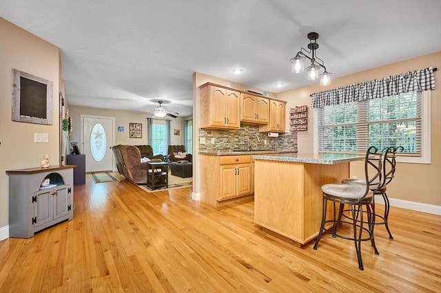 kitchen with light brown cabinetry, light wood-type flooring, plenty of natural light, and baseboards