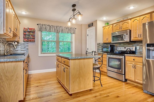 kitchen featuring appliances with stainless steel finishes, a sink, a kitchen island, a kitchen breakfast bar, and light wood-style floors