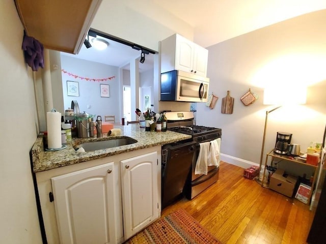 kitchen with light stone countertops, light wood-type flooring, appliances with stainless steel finishes, white cabinets, and a sink