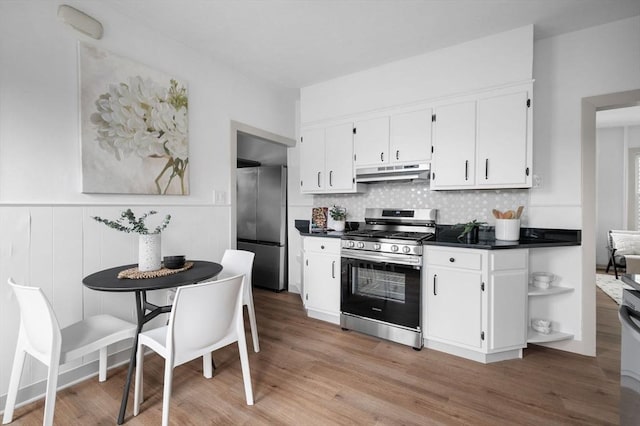 kitchen featuring under cabinet range hood, dark countertops, stainless steel appliances, white cabinets, and decorative backsplash