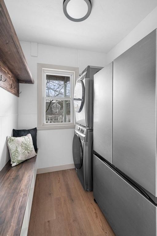 laundry area featuring light wood finished floors, laundry area, stacked washing maching and dryer, and baseboards