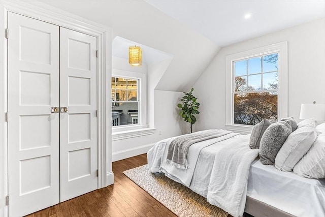 bedroom featuring dark wood-style floors, lofted ceiling, a closet, and baseboards