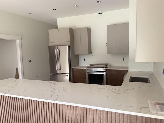 kitchen with gray cabinetry, high end appliances, light stone countertops, kitchen peninsula, and sink