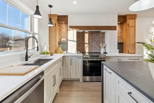 kitchen featuring light wood-type flooring, pendant lighting, a sink, backsplash, and stainless steel appliances