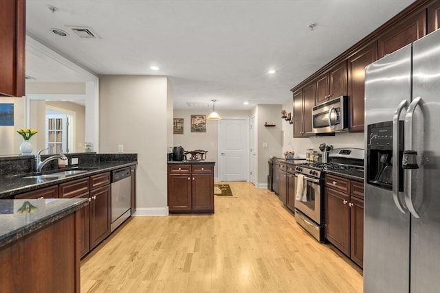 kitchen featuring sink, light hardwood / wood-style flooring, appliances with stainless steel finishes, dark stone countertops, and hanging light fixtures