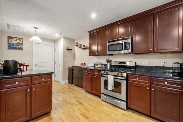 kitchen featuring appliances with stainless steel finishes, light hardwood / wood-style floors, hanging light fixtures, and dark stone countertops