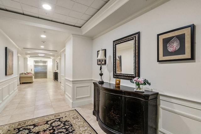 corridor with a tray ceiling, light tile patterned floors, crown molding, and elevator