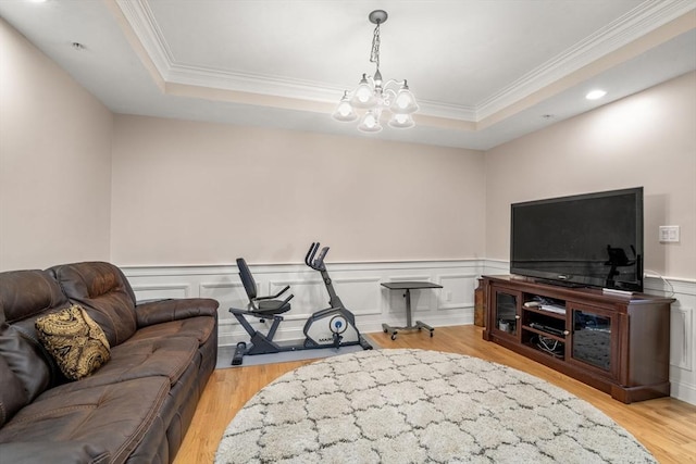 living room with ornamental molding, a raised ceiling, light hardwood / wood-style floors, and a notable chandelier