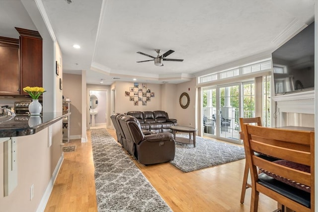 living room featuring a tray ceiling, crown molding, light hardwood / wood-style flooring, and ceiling fan