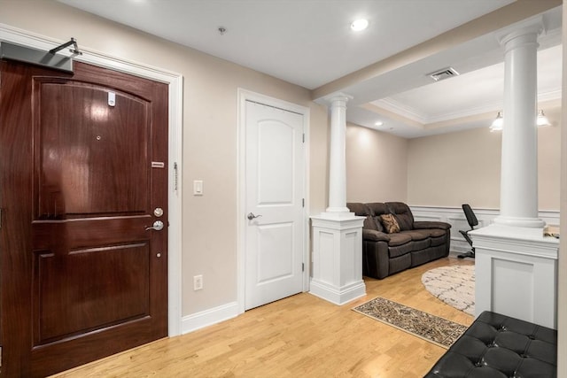 foyer with decorative columns, crown molding, a tray ceiling, and light hardwood / wood-style flooring