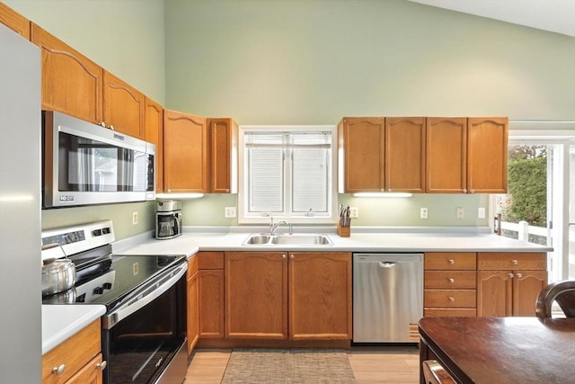 kitchen with stainless steel appliances, a sink, high vaulted ceiling, light wood-type flooring, and light countertops