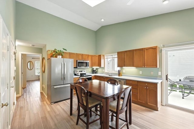 kitchen featuring appliances with stainless steel finishes, high vaulted ceiling, a sink, light countertops, and light wood finished floors