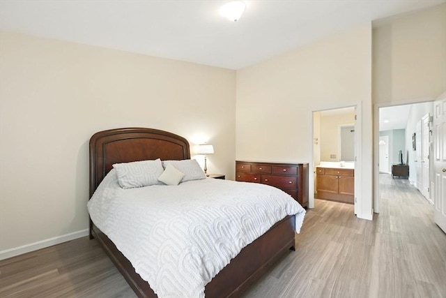 bedroom with light wood finished floors, baseboards, and ensuite bath