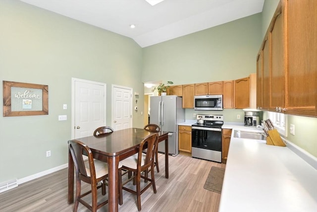 kitchen featuring appliances with stainless steel finishes, high vaulted ceiling, a sink, light countertops, and light wood-style floors