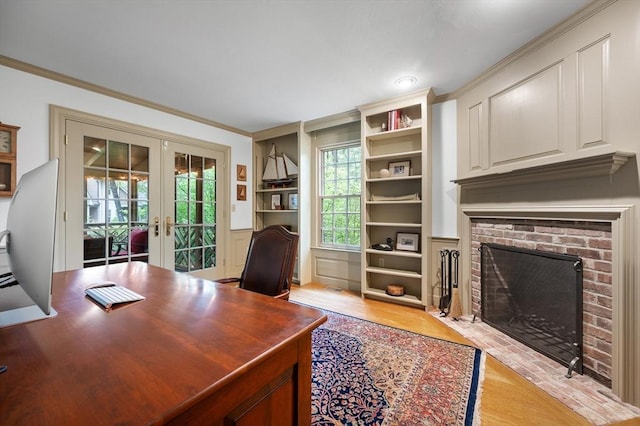 office space featuring french doors, a brick fireplace, light wood-type flooring, ornamental molding, and built in shelves