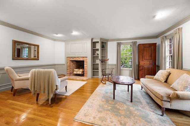 living area with ornamental molding, light wood-style floors, a fireplace, wainscoting, and a decorative wall