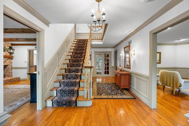 stairs featuring wood-type flooring, a chandelier, a decorative wall, crown molding, and wainscoting