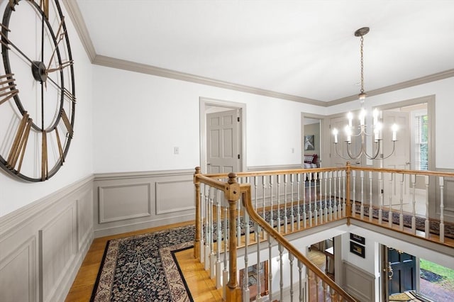 hallway with an upstairs landing, a chandelier, light wood-style flooring, ornamental molding, and a wainscoted wall