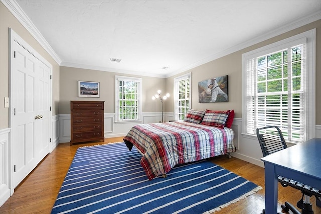 bedroom with ornamental molding, wood finished floors, a wainscoted wall, and a decorative wall