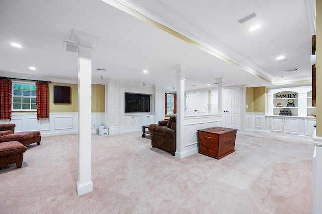 living area with crown molding, ornate columns, light carpet, a decorative wall, and a wainscoted wall