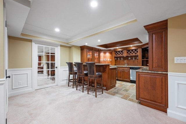 indoor wet bar with a tray ceiling, a decorative wall, stainless steel dishwasher, a wainscoted wall, and ornamental molding
