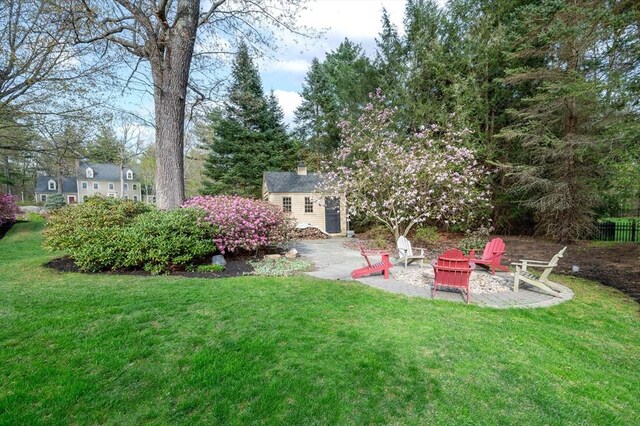 view of green lawn featuring an outdoor structure, a fire pit, and a patio