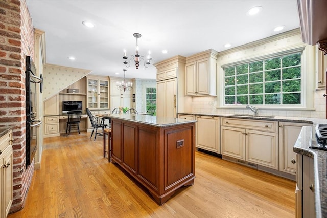 kitchen featuring cream cabinetry, a sink, a chandelier, light stone countertops, and a center island