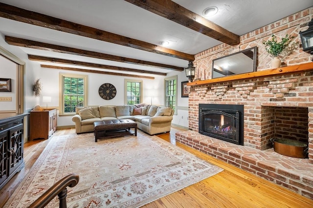 living room with wood-type flooring, a brick fireplace, beamed ceiling, and baseboards