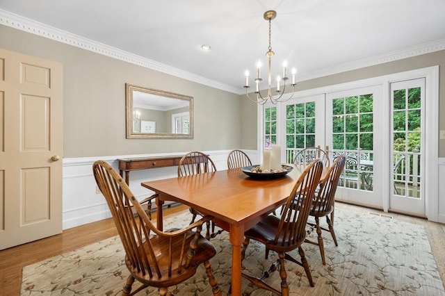 dining room featuring a chandelier, light wood-style floors, ornamental molding, a wainscoted wall, and french doors