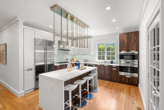 42 Coolidge St Unit 42, Brookline, MA 02446 - kitchen featuring stainless steel appliances, modern cabinets, wall chimney exhaust hood, light countertops, and crown molding