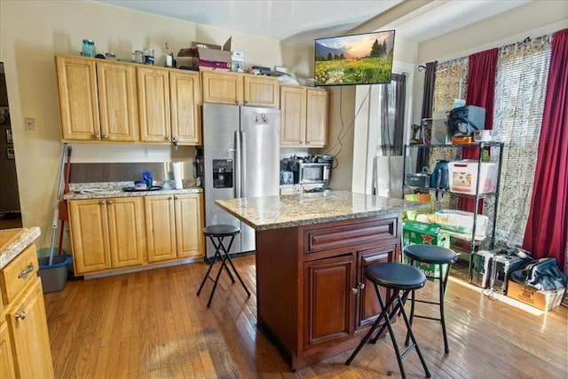 kitchen featuring stainless steel appliances, a center island, light wood-style flooring, a kitchen bar, and light stone counters