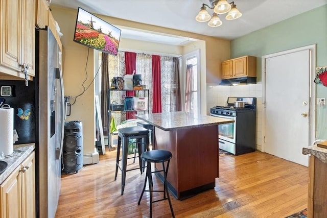 kitchen featuring light wood finished floors, under cabinet range hood, a chandelier, a kitchen bar, and appliances with stainless steel finishes