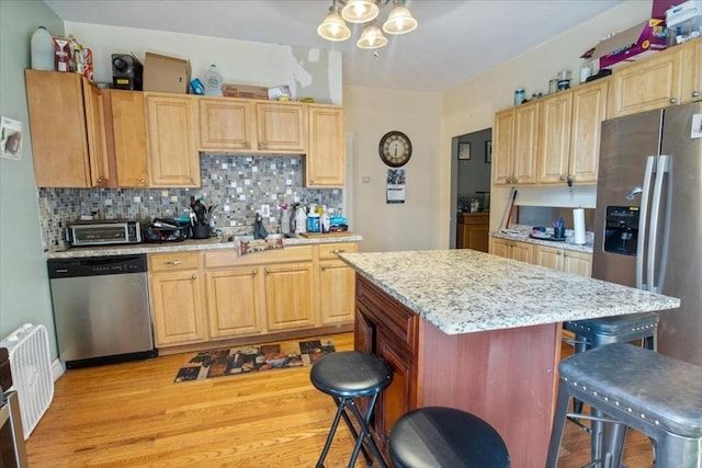 kitchen with light wood-type flooring, a chandelier, decorative backsplash, a breakfast bar, and appliances with stainless steel finishes