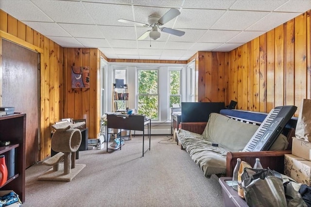 sitting room with wooden walls, carpet flooring, and ceiling fan