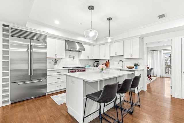 280 W 5th St Unit 101, Boston, MA 02127 - kitchen with stainless steel built in fridge, wall chimney range hood, light countertops, dark wood-type flooring, and a kitchen bar
