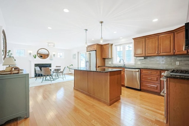 kitchen featuring pendant lighting, appliances with stainless steel finishes, backsplash, a kitchen island, and light wood-type flooring