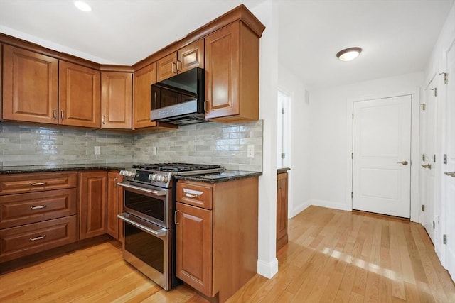 kitchen with backsplash, light hardwood / wood-style floors, dark stone counters, and range with two ovens