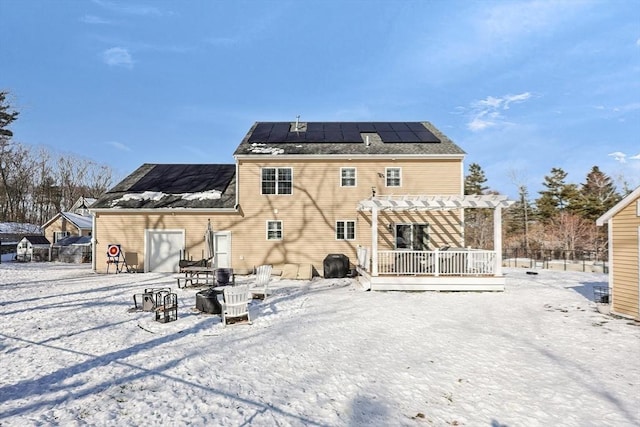 snow covered house with a wooden deck, a pergola, and solar panels